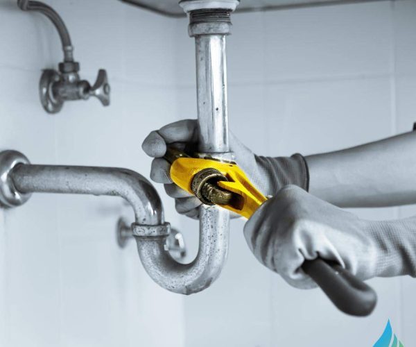 professional with gloves working on plumbing leak under sink